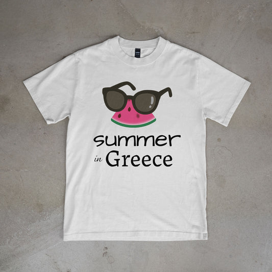 White t-shirt with watermelon and sunglasses graphic and 'summer in Greece' text on a concrete surface.