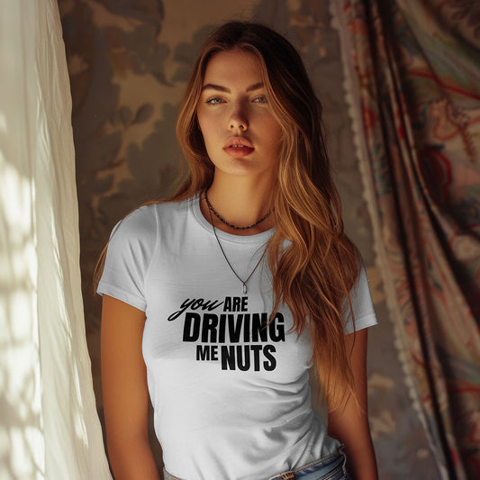 Woman wearing a white t-shirt with text "you are driving me nuts" in a room with curtains.