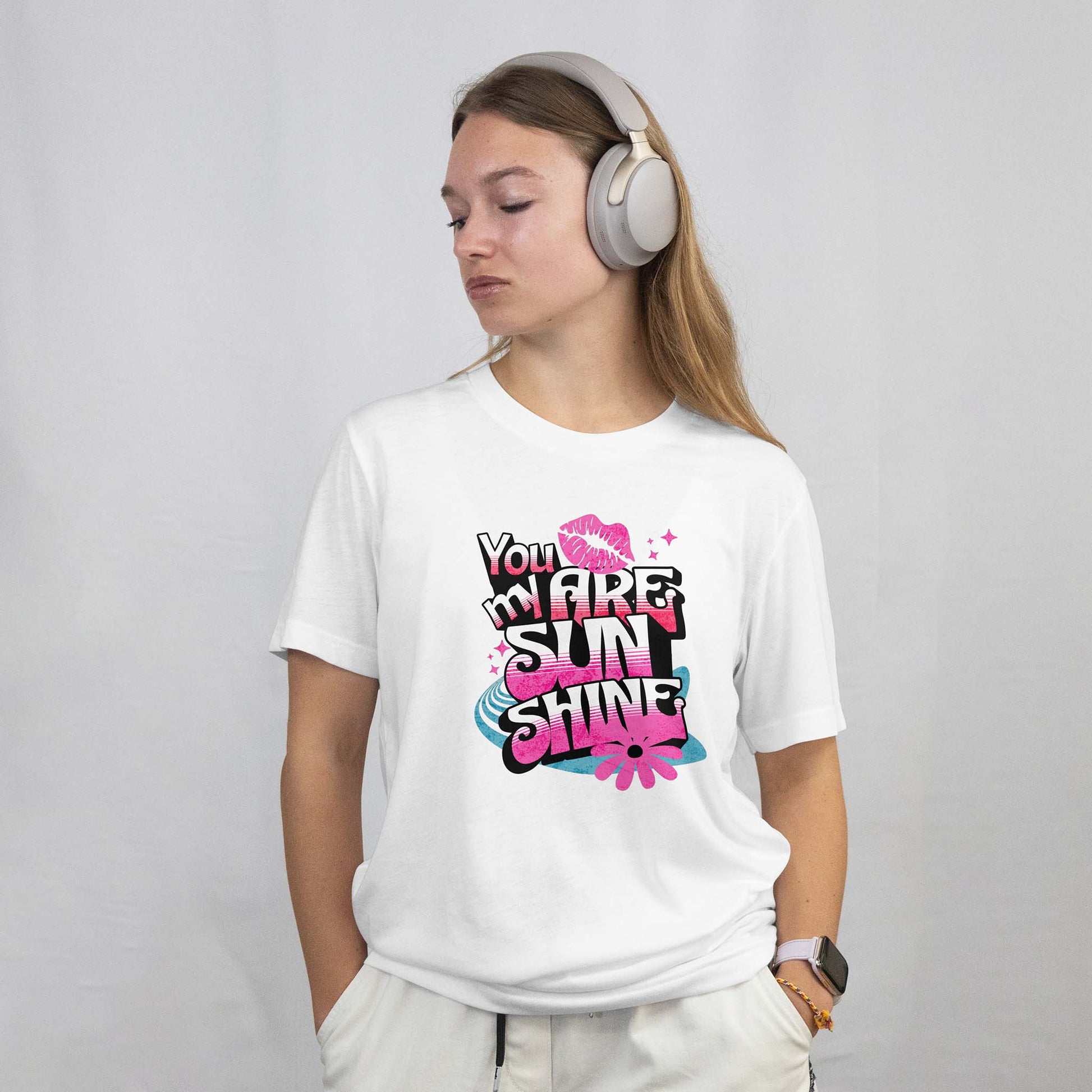 Woman wearing a white t-shirt with colorful text design and headphones on a plain background